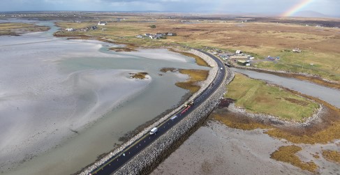 Aerial view of a road winding through a coastal landscape with a partial rainbow in the sky