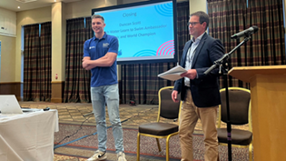 2 men standing presenting in front of a big screen