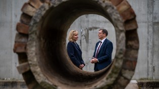 Two people pose as camera lense focuses from a far away distance through a water pipe
