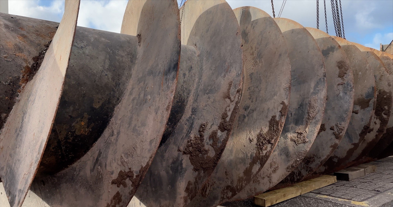 A massive 9 tonne metal screw sits on top of the ground having been removed from an underground waste water pumping station.