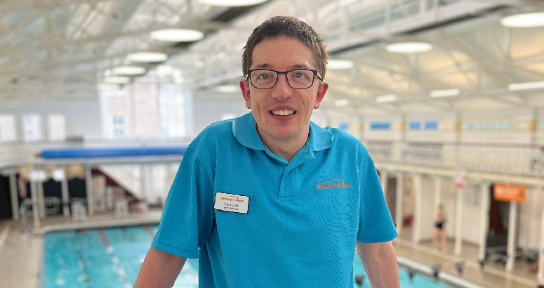 Scott Quin, a swim teacher at Edinburgh Leisure, standing in front of a swimming pool inside a brightly lit leisure centre