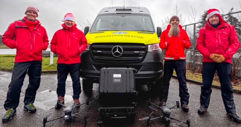 4x members of the Lomond Mountain Rescue Team standing in front of their van at Milngavie Reservoir wearing santa hats, with their new Search and Rescue Drones on the ground in front of them.